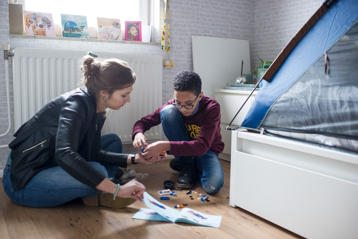 Vrouw spelt met jongen met lego op de grond in slaapkamer