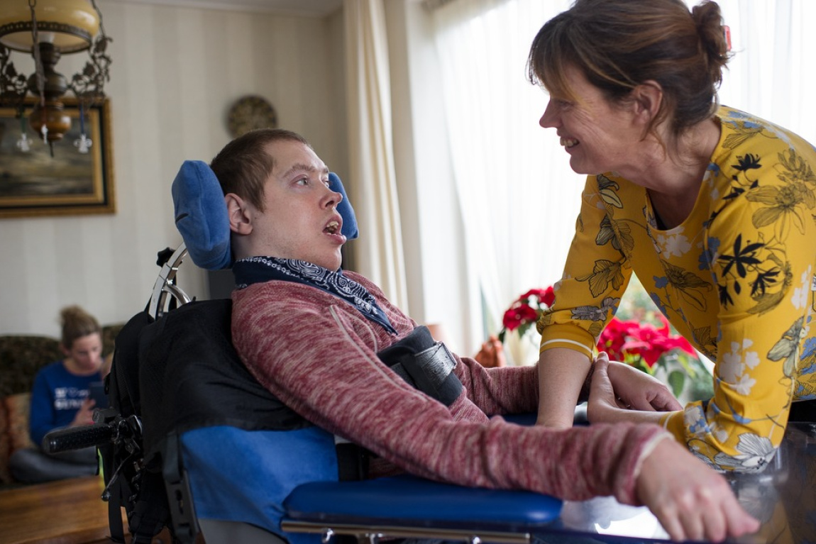 Man in rolstoel kijkt naar lachende vrouw die leunt op zijn rolstoel
