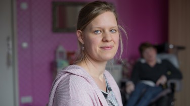 Vrouw kijkt in camera, vrouw in rolstoel op de achtergrond