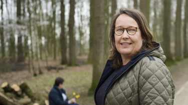 twee vrouwen in bos, een kijkt in camera, ander op een boomstam ver weg, kijkt weg