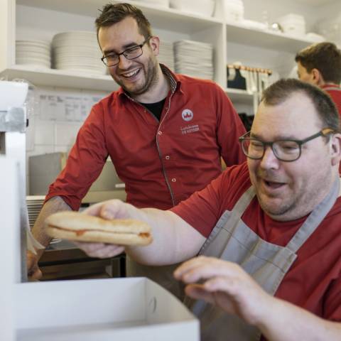 Man pakt broodjes in in doos, andere man kijkt lachend toe