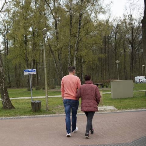 Man en vrouw lopen gearmd over een weg in het groen