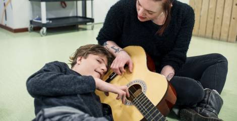 Jongen ligt met oor op gitaar, vrouw tokkelt op gitaar