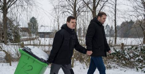 Twee mannen lopen buiten hand in hand, een met container