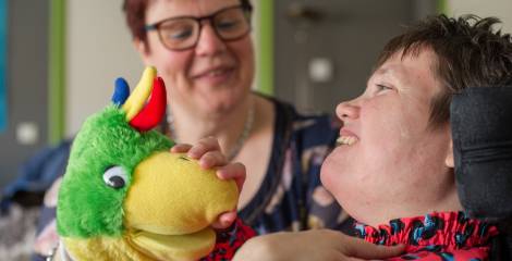 Vrouw in rolstoel lacht om vrouw met knuffel